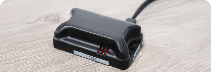 LevelTag leveling device with X-axis indicator and charging cable connected, showing red LED lights on a wooden surface